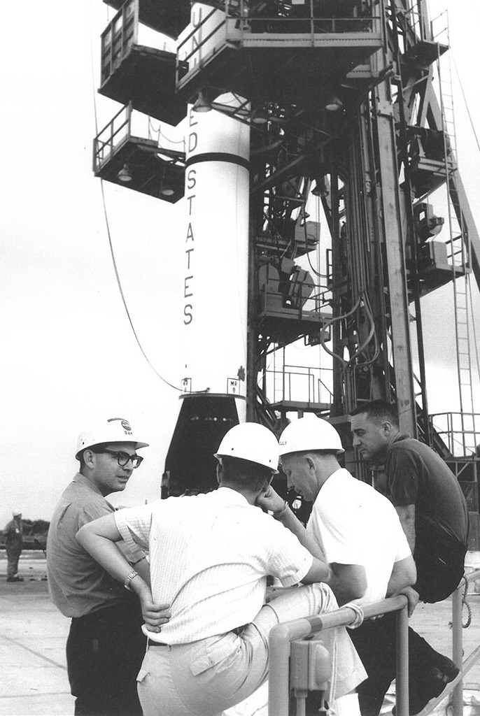 Sam Beddingfield, Gus Grissom, and two other men talk near a rocket on a launchpad