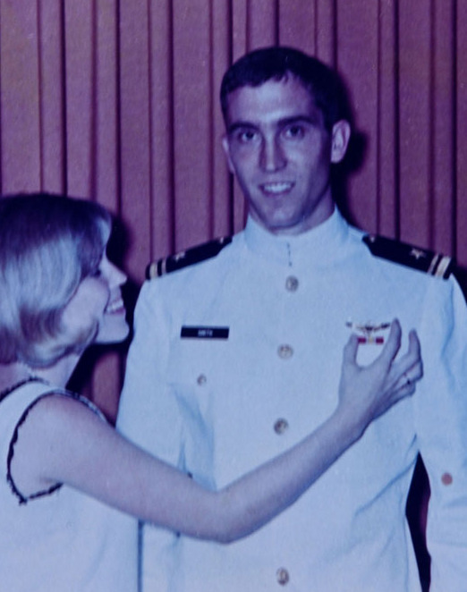 Michael Smith in his naval dress uniform getting his wings pinned on by a woman