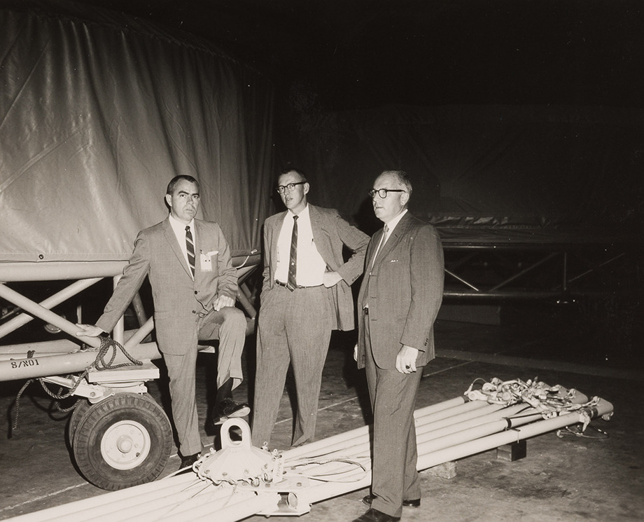 Arthur Case and two other men stand in suits in front of NASA equipment