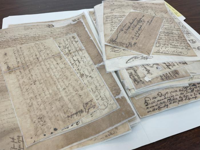 stack of old documents of varying sizes lying on a wooden desk
