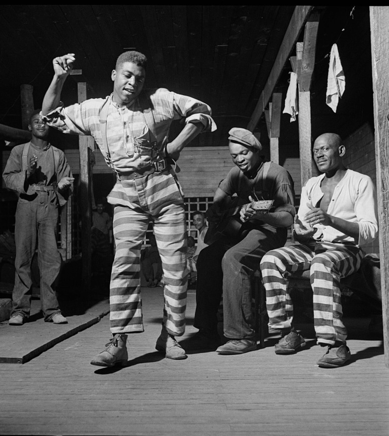 One incarcerated man dances while another plays guitar.