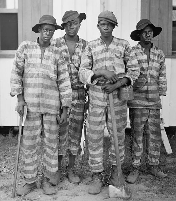 Four African American incarcerated laborers standing together holding axes. The men are chained together.
