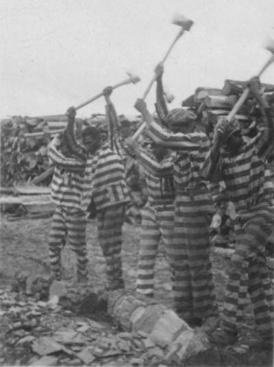 Incarcerated men using axes to chop wood at a prison labor camp in South Carolina, circa 1934